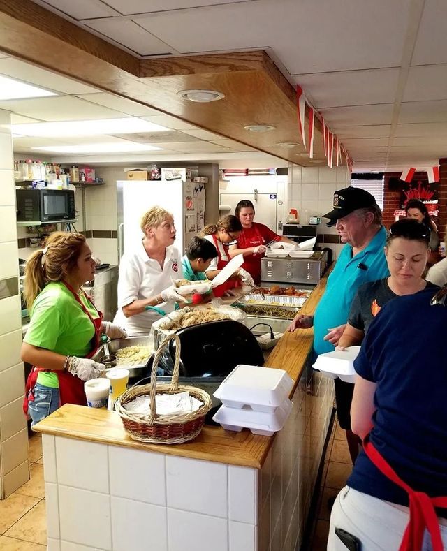 People serving and receiving food at a buffet counter in a busy indoor dining area