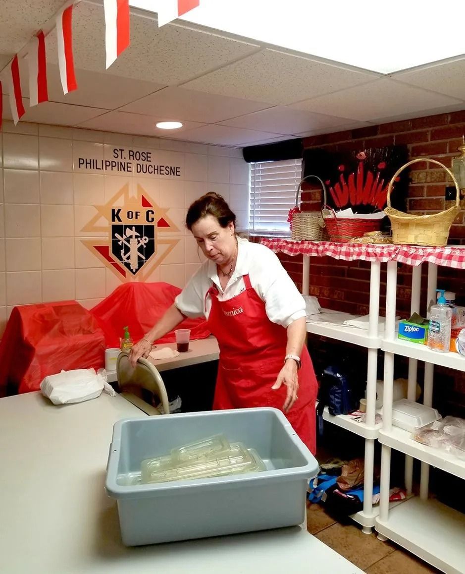 Person in a red apron preparing food in a kitchen with shelves and a large gray tub.