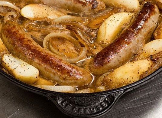Sausages and onions simmering in a skillet with a rich brown sauce