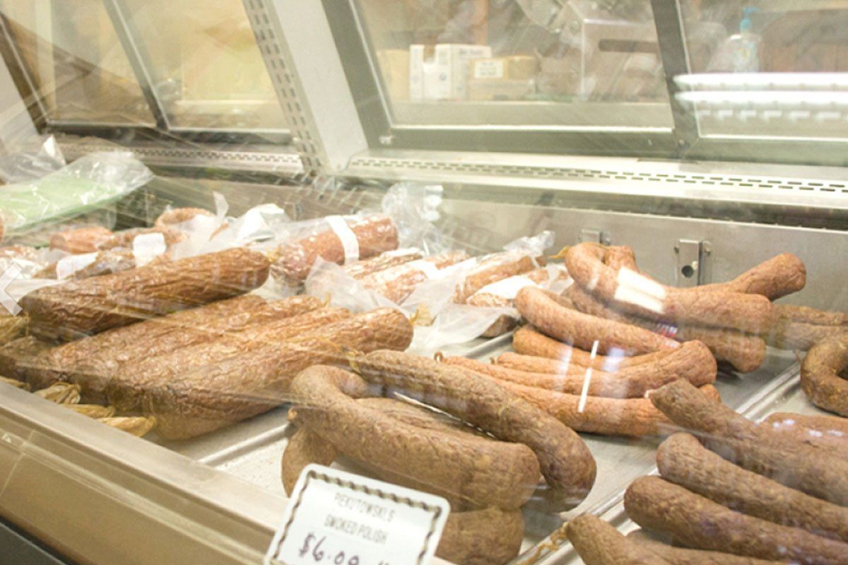 Assorted sausages and cured meats displayed in a deli case behind glass.