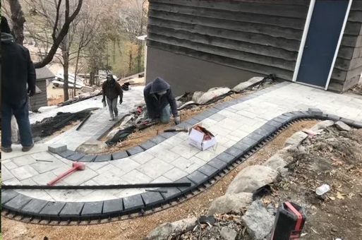 A group of men are working on a sidewalk in front of a house