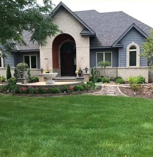 A large house with a lush green lawn and a fountain in front of it