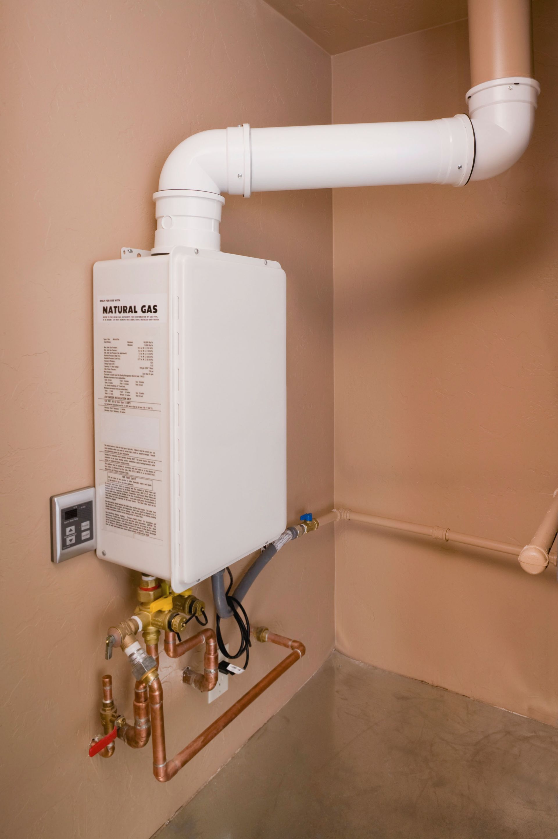 Tankless water heater mounted on a beige wall with copper pipes and white vent.