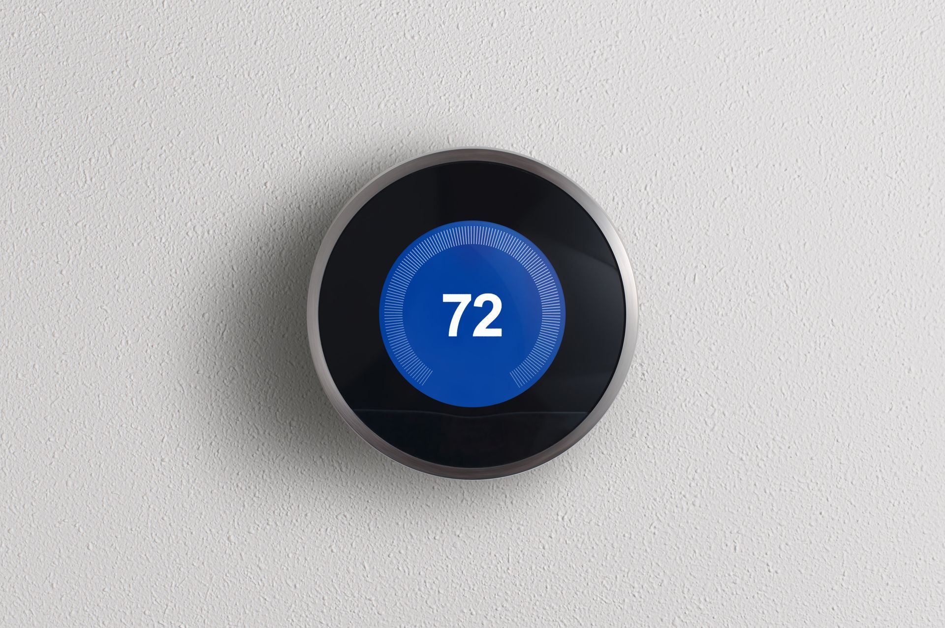 Smart thermostat with a blue display showing the temperature 72 degrees, mounted on a white wall.
