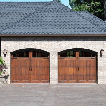 Two brown wooden garage doors under arched brick facade, gray roof.