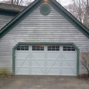 White garage door with windows, accented with green trim, on a weathered gray building.