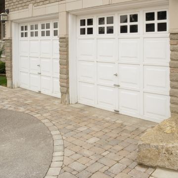 Two white garage doors with glass panels, stone exterior, and brick pathway.