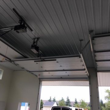 Garage ceiling with two overhead door openers, door panels, and an open garage door.