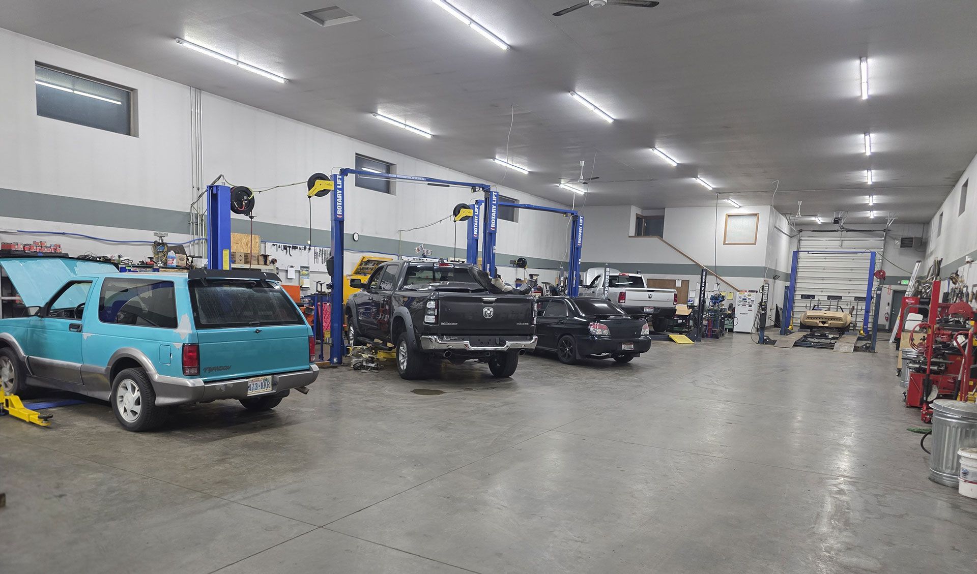 A wide-angle view of a well-lit auto repair shop with multiple vehicles parked under service lifts.