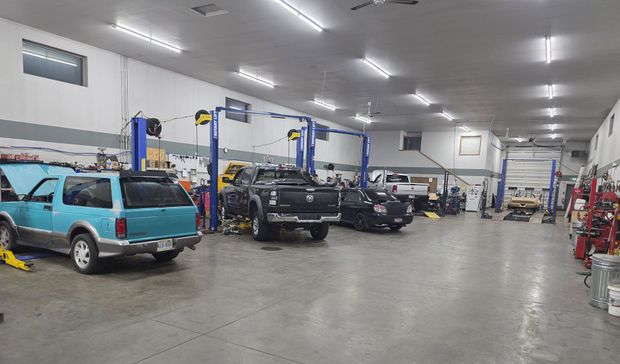 An auto repair shop interior with several cars parked in bays under bright overhead lights.