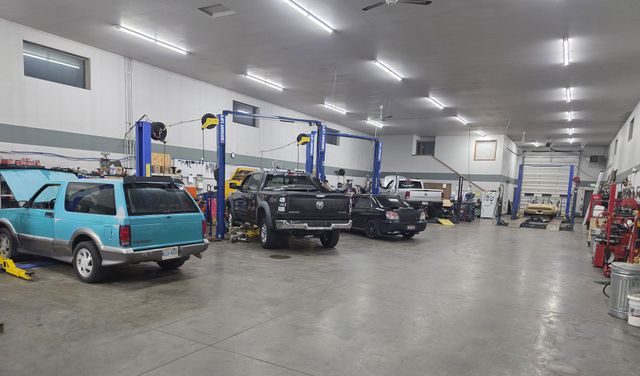 An auto repair shop interior with several cars parked in bays under bright overhead lights.