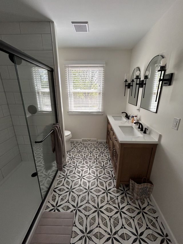 Modern bathroom with glass shower, patterned tile floor, and double vanity under wall mirrors