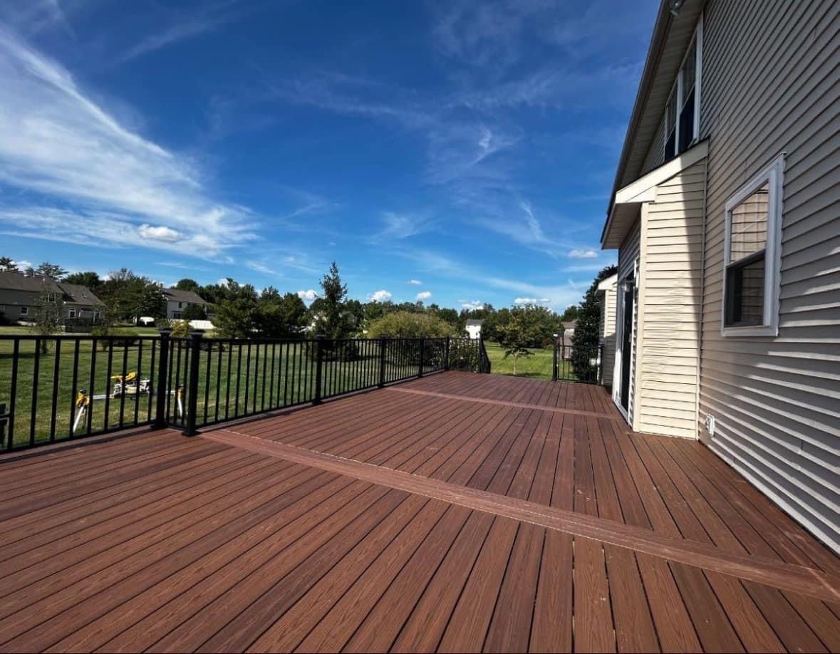 Wooden deck with black railing beside a beige house under a blue sky