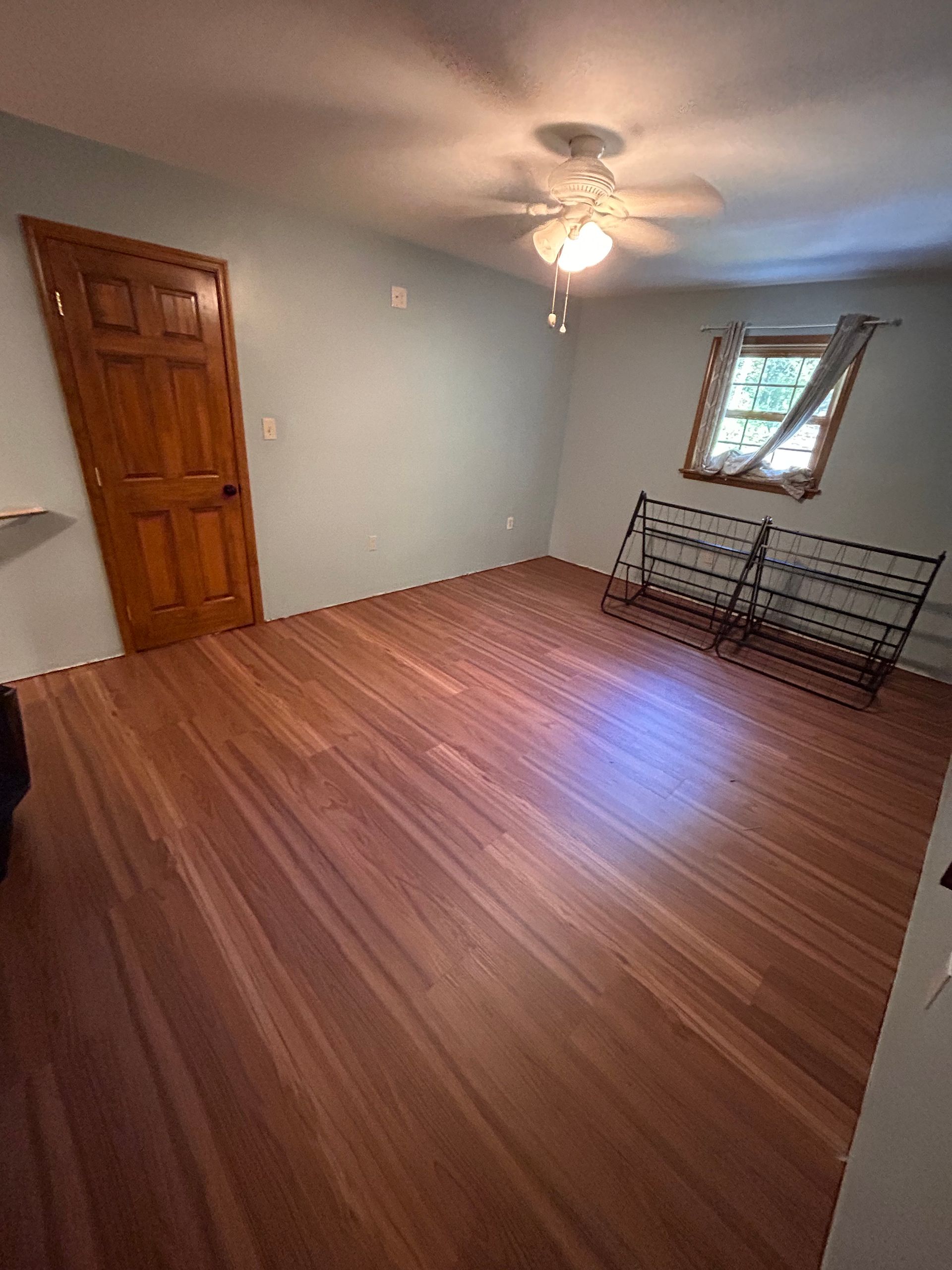 Empty bedroom with wood floor, ceiling fan, closet door, and a window with blinds.