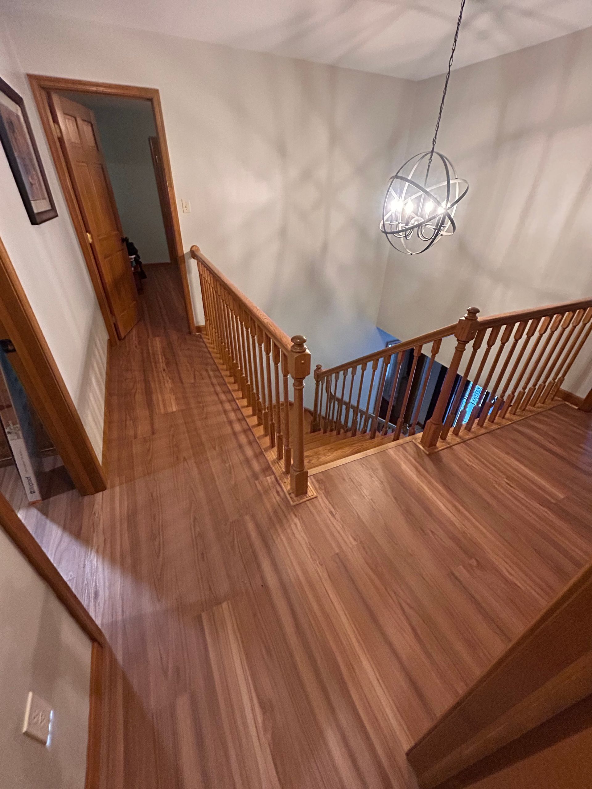 Upper landing with wooden railings and stairs, viewed from a hallway, with a hanging light fixture overhead