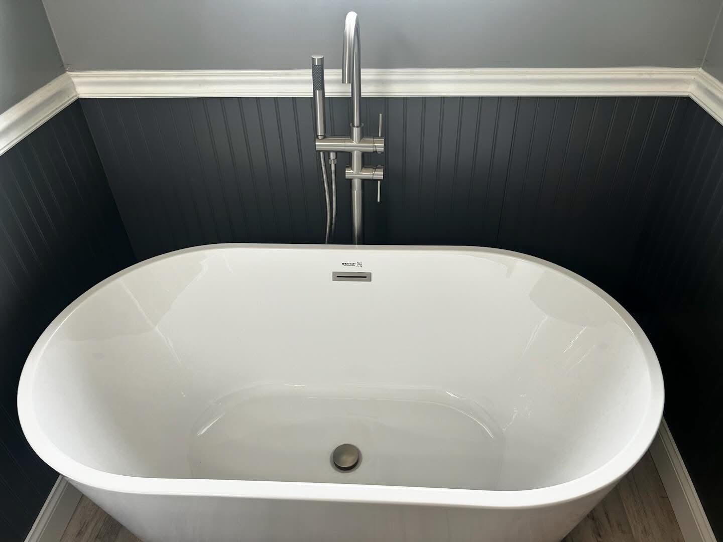 Freestanding white bathtub in a dark gray bathroom with a chrome shower fixture