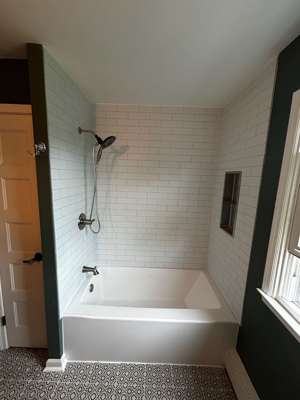 Small bathroom with a white bathtub, white tile surround, and dark green walls.