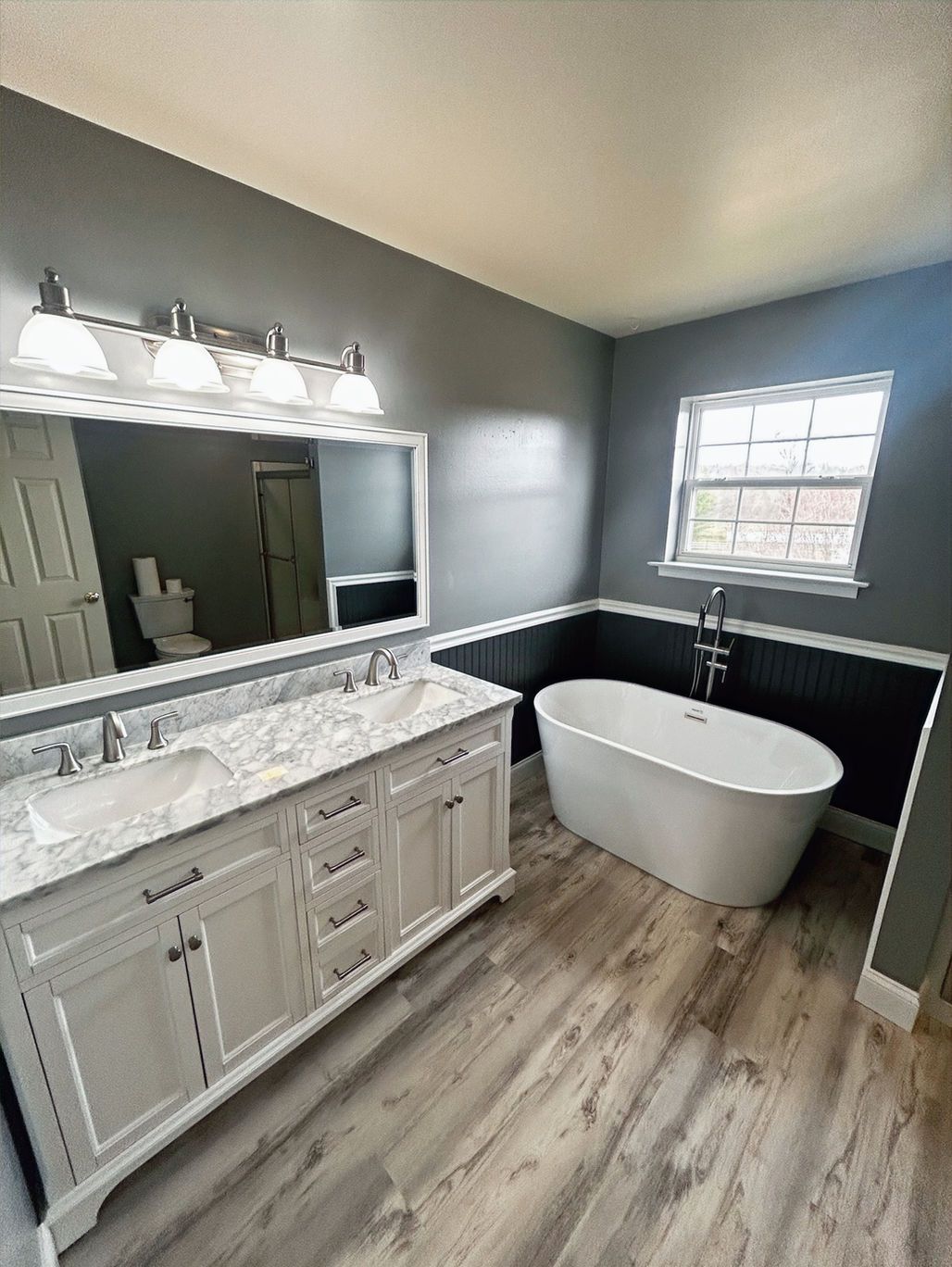Modern bathroom with double vanity, freestanding tub, gray walls, and wood-look flooring