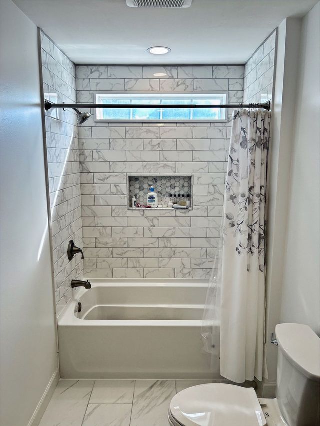 Small white tiled bathroom with a bathtub, shower curtain, and toilet.