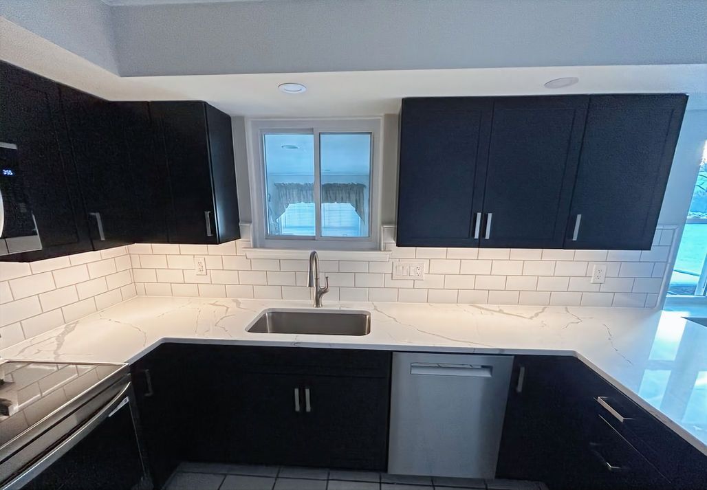 Modern kitchen with black cabinets, white tile backsplash, window above sink, and stainless dishwasher