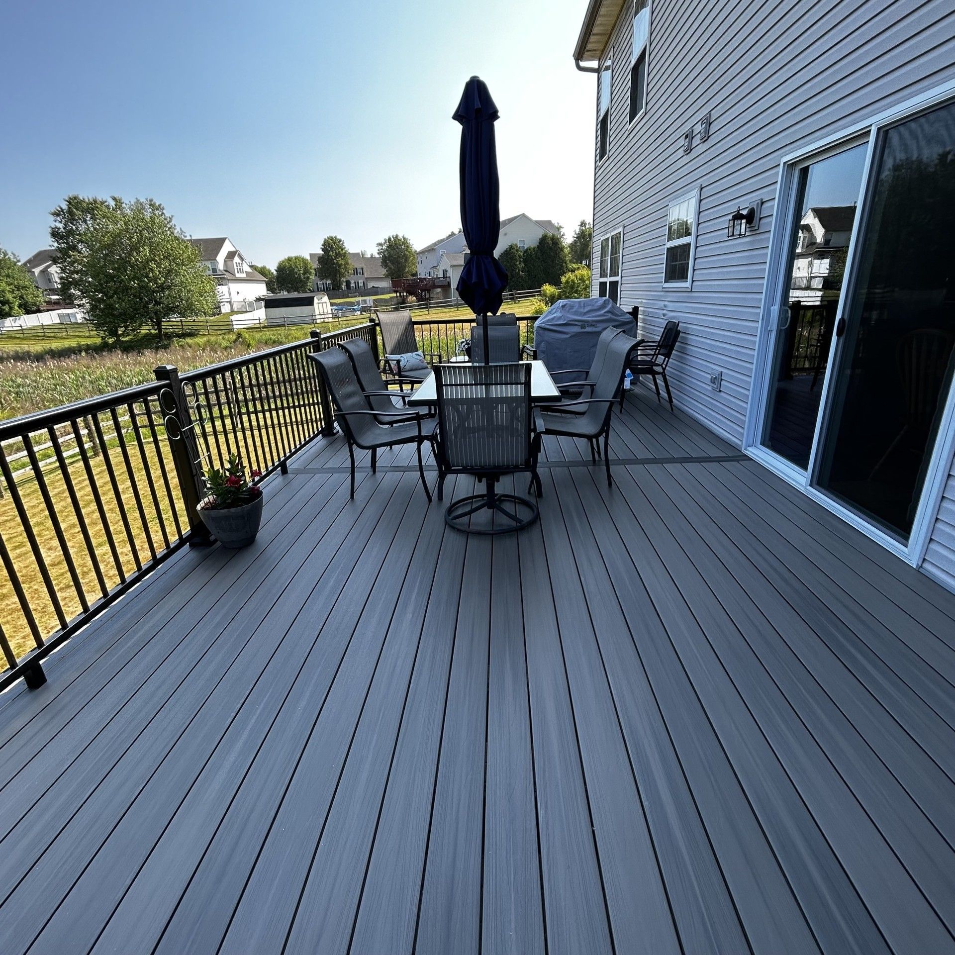 Spacious gray backyard deck with patio table, chairs, umbrella, and potted plants beside a house