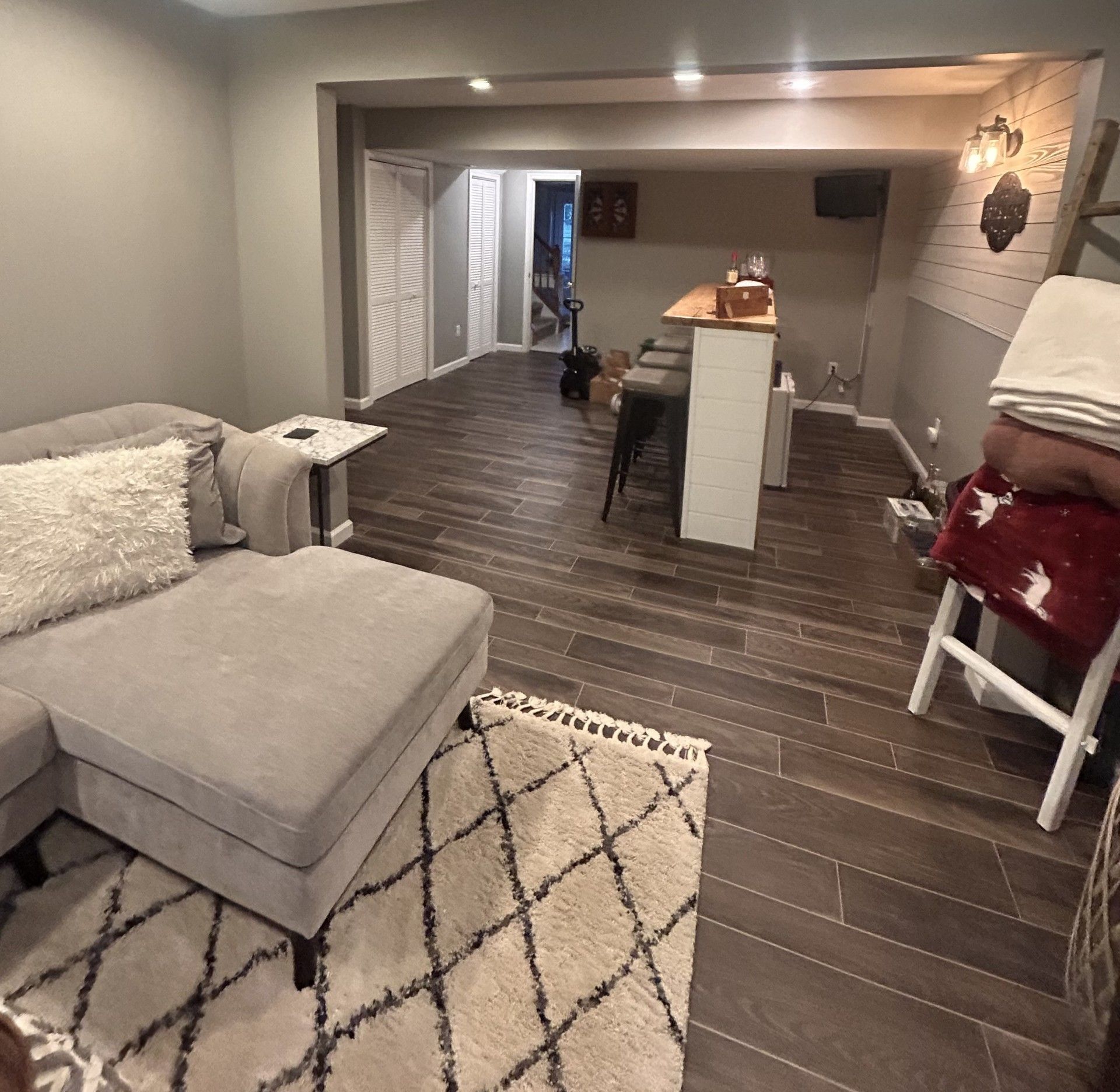 Modern living room with gray sectional, dark wood floors, area rug, and a bar counter leading to another room