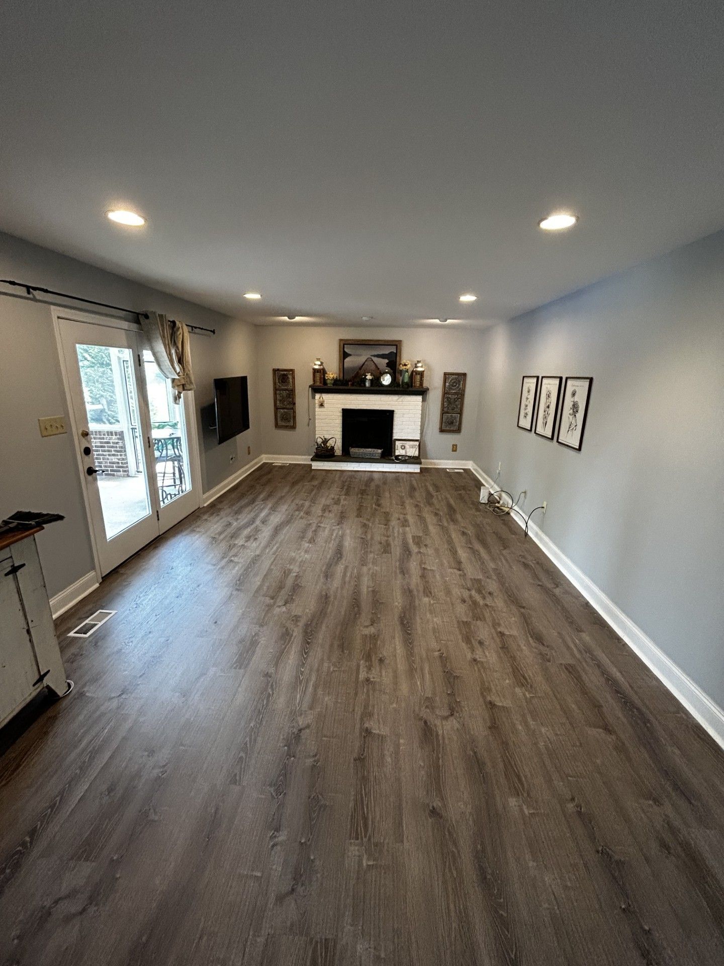 Empty living room with wood floors, gray walls, recessed lights, and a fireplace with TV above it