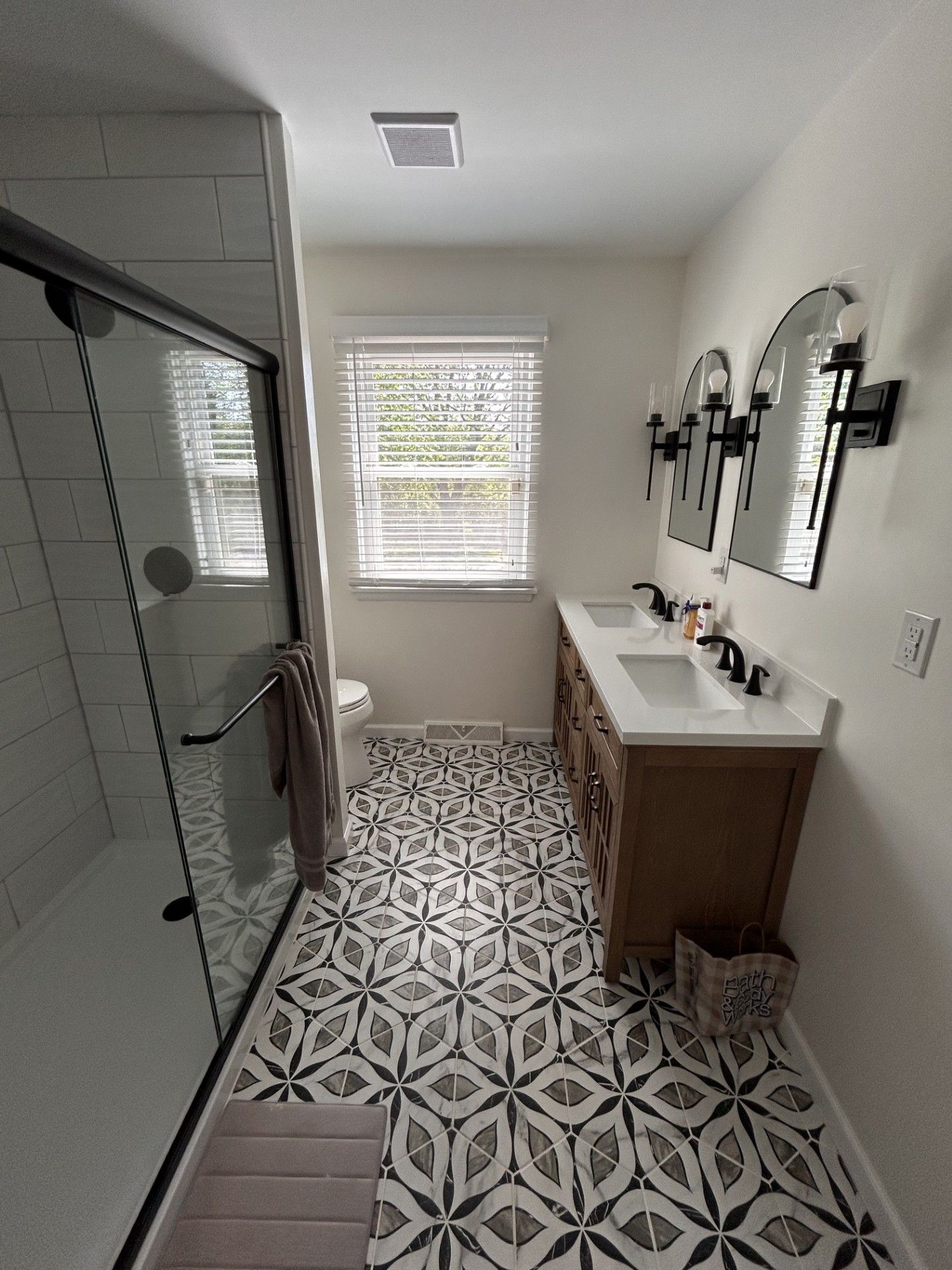 Modern bathroom with glass shower, patterned tile floor, and double vanity under arched mirrors.