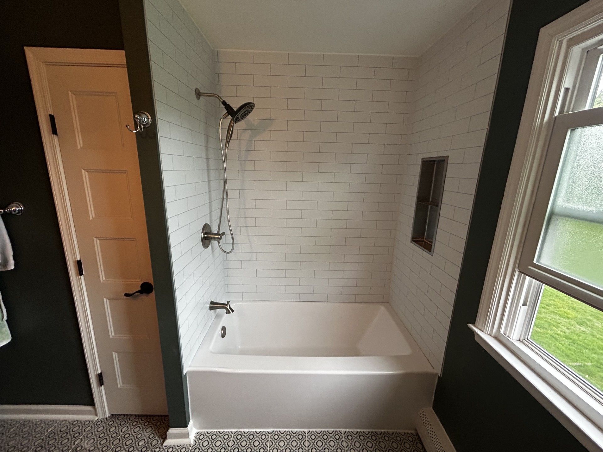 Bathroom with white bathtub, tiled shower wall, and window letting in daylight