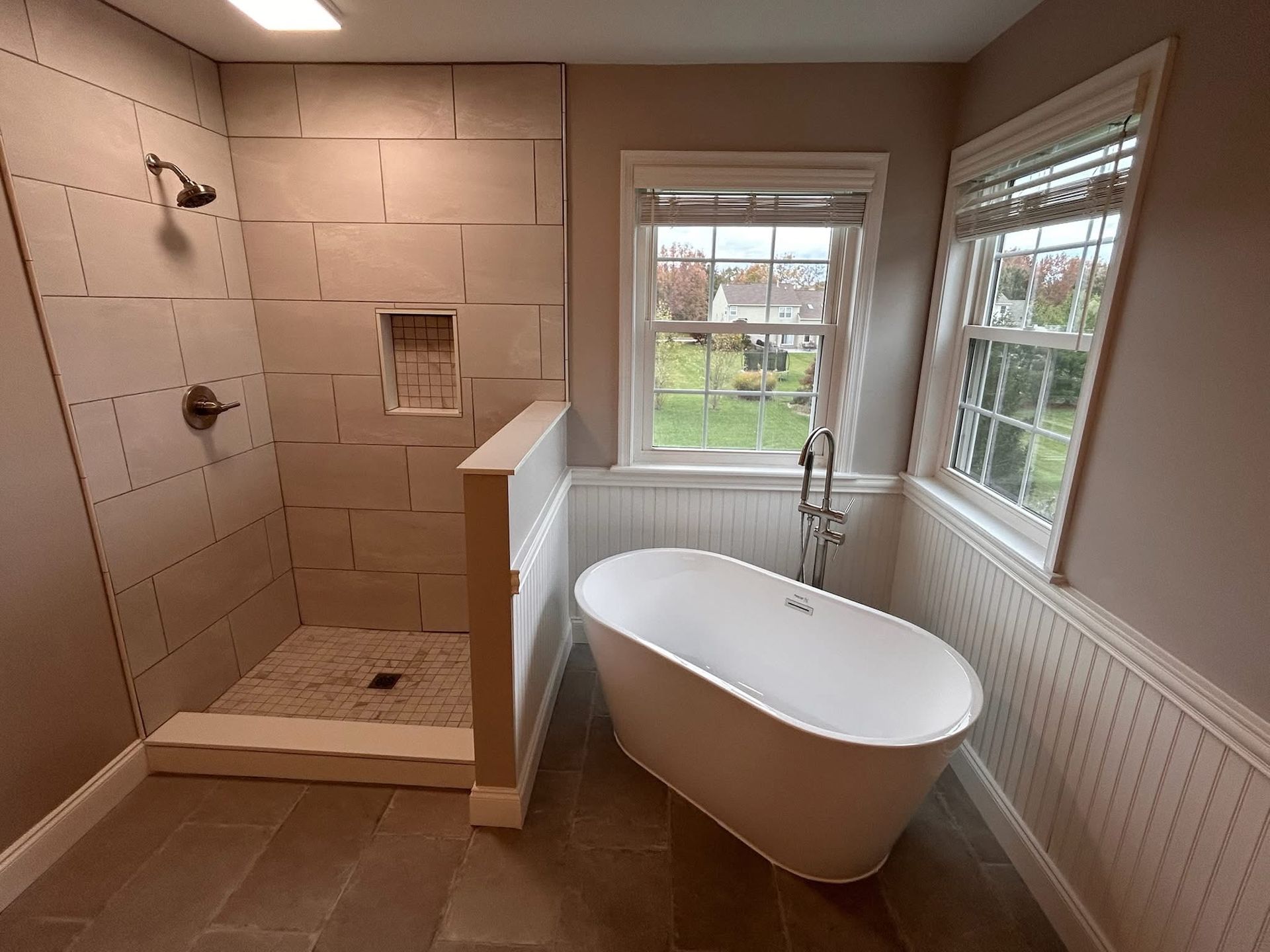 Bathroom with walk-in shower, freestanding tub, window, and white wainscoting.