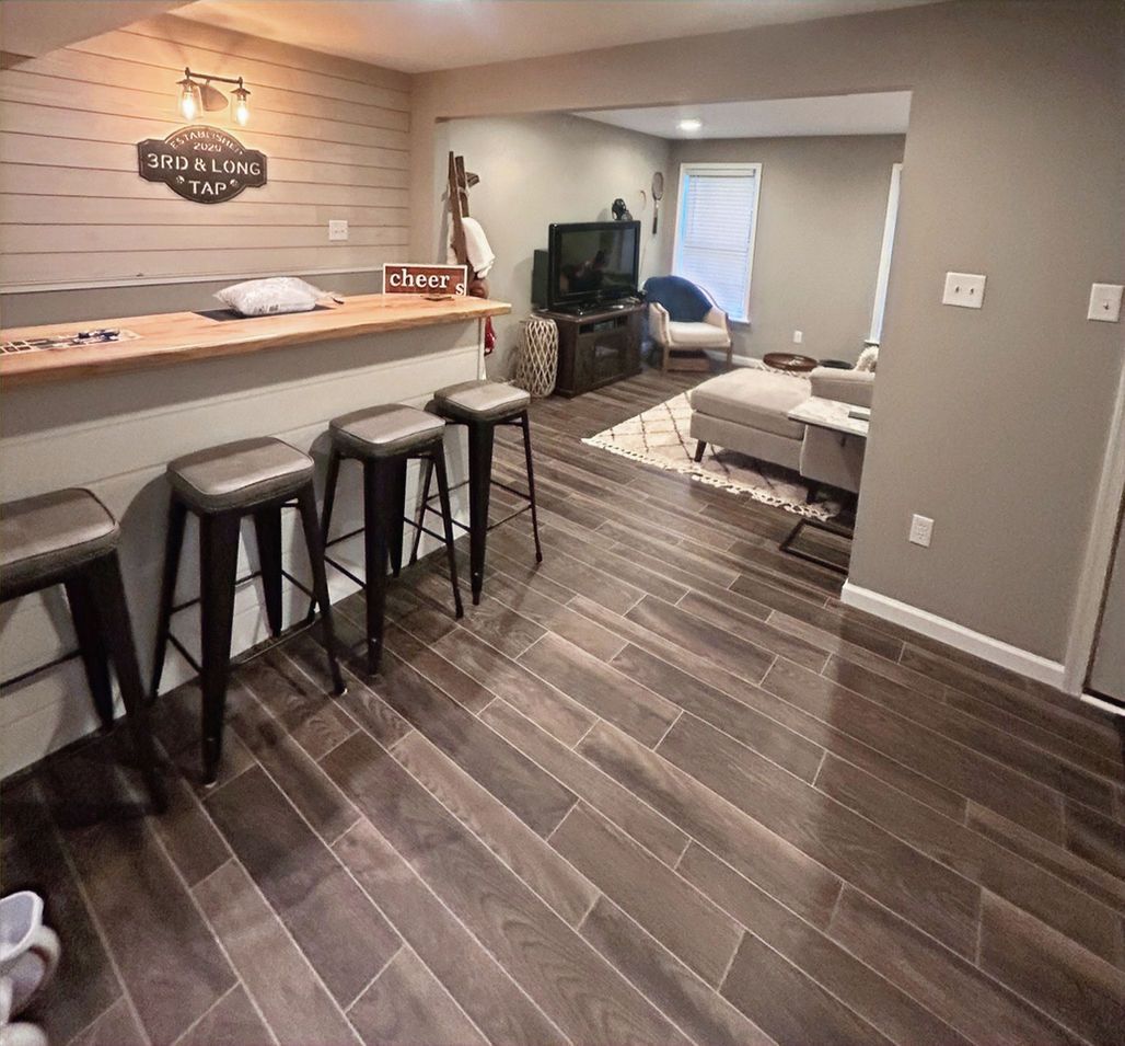 Basement living room with bar stools, gray walls, wood floor, and a TV area in the back