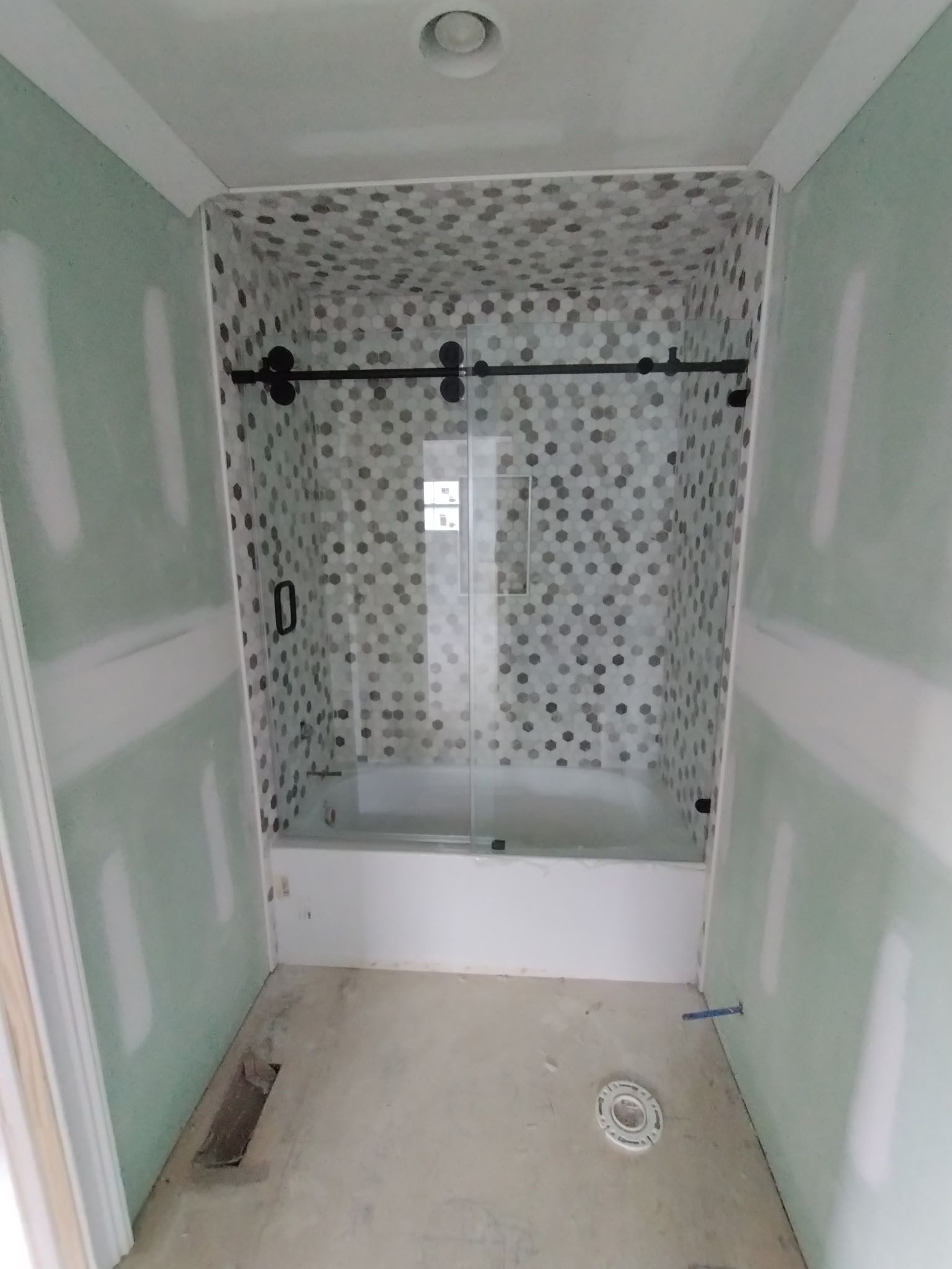 Bathroom under construction featuring a white bathtub, tiled shower walls with a sliding glass door, and bare wall panels. 