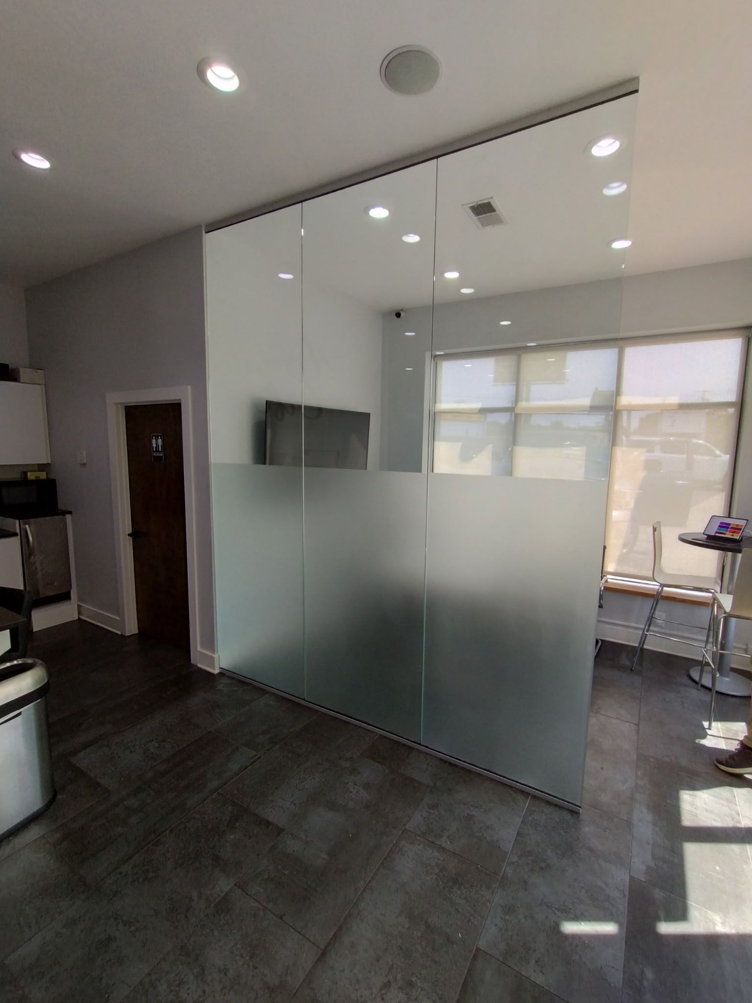 Interior view of a room featuring a large, floor-to-ceiling glass wall partition with a frosted middle section. 
