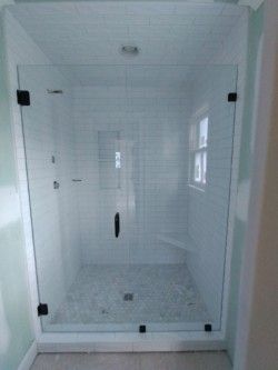 A glass shower door installed in a tiled walk-in shower with white subway tiles and a stone-patterned floor. 