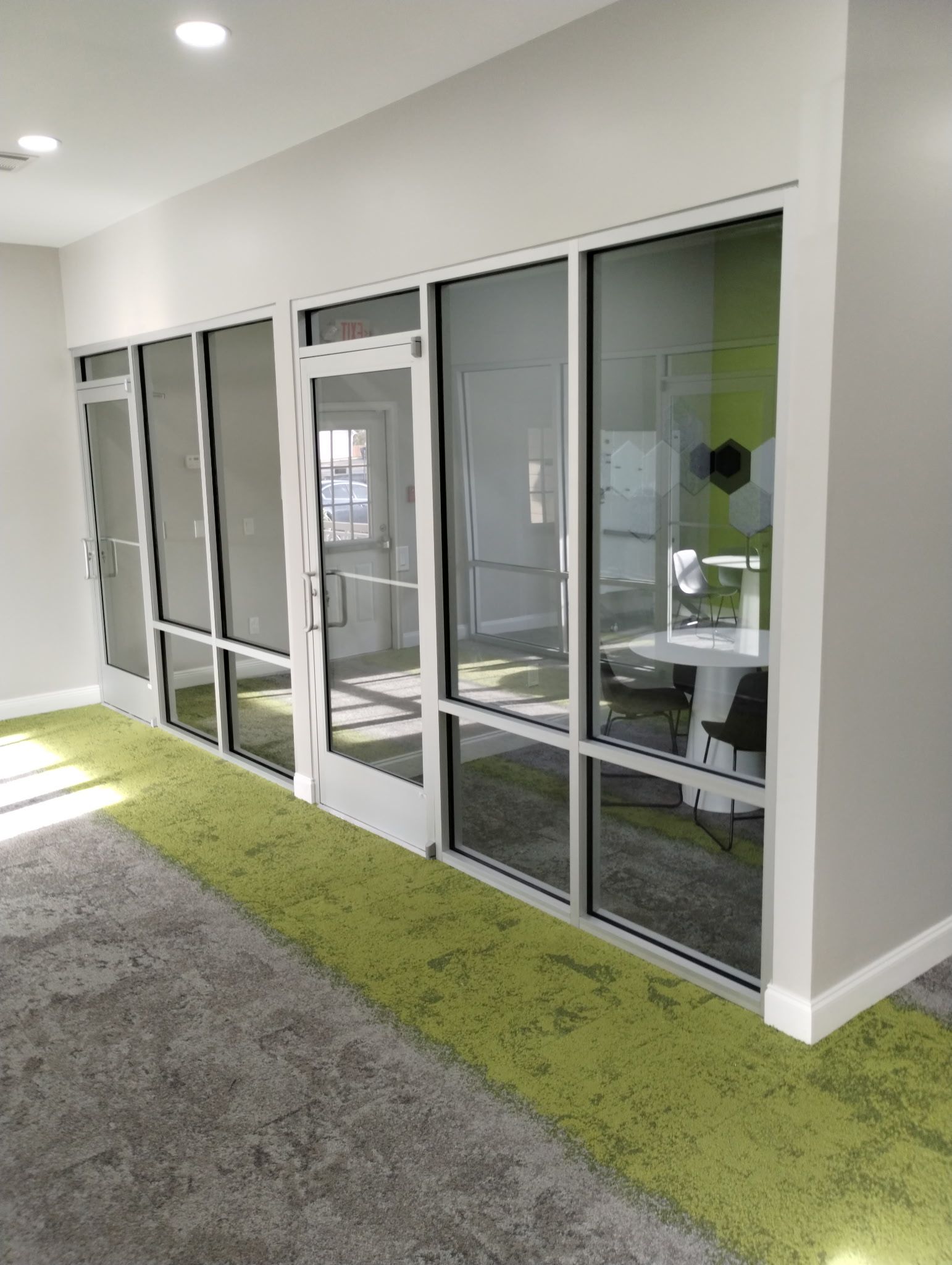 An interior office corridor with a glass-paneled wall, a door, green accent carpeting, and gray walls.