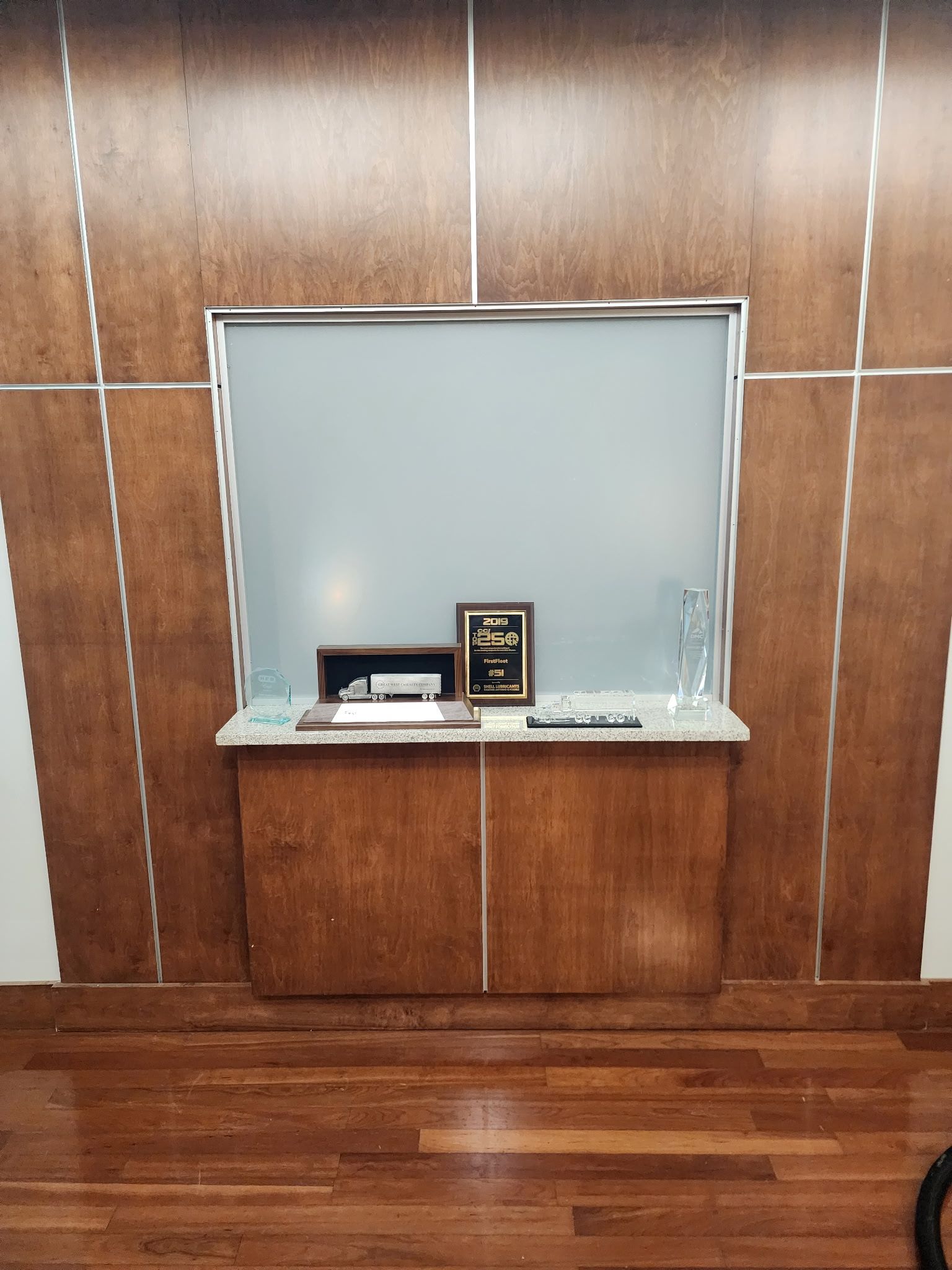 A wood-paneled wall features a central recessed window shelf displaying a small truck model, a plaque, and a glass award. 