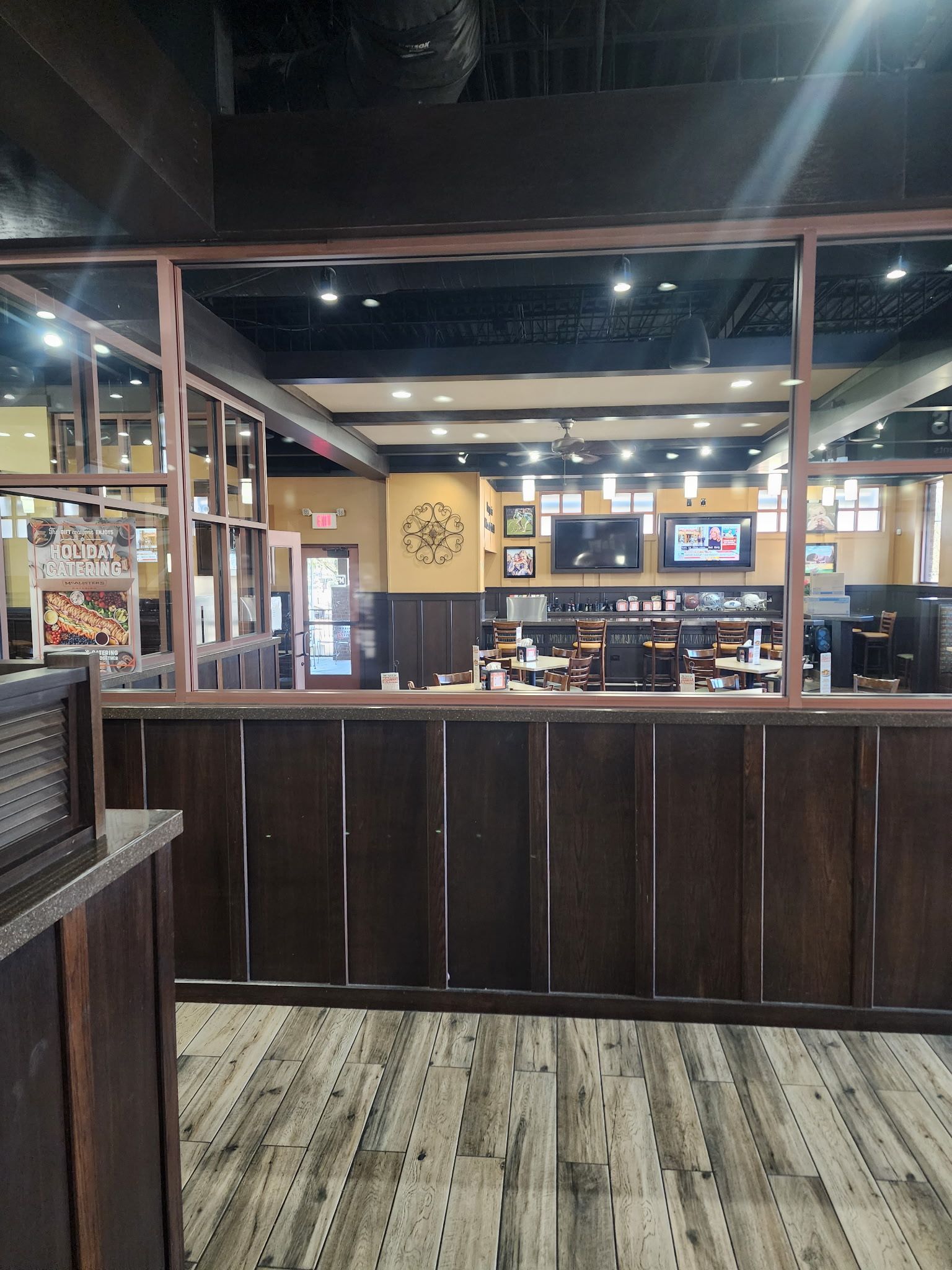 Interior view of an empty restaurant bar area with wood paneling, wood-look flooring, and TVs on the back wall. 
