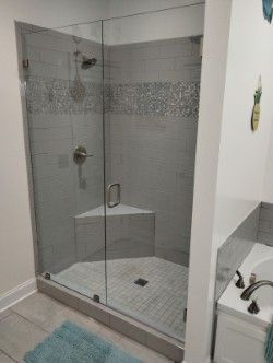 A glass-enclosed shower with grey tiled walls, a built-in bench, and a silver shower head fixture in a modern bathroom. 