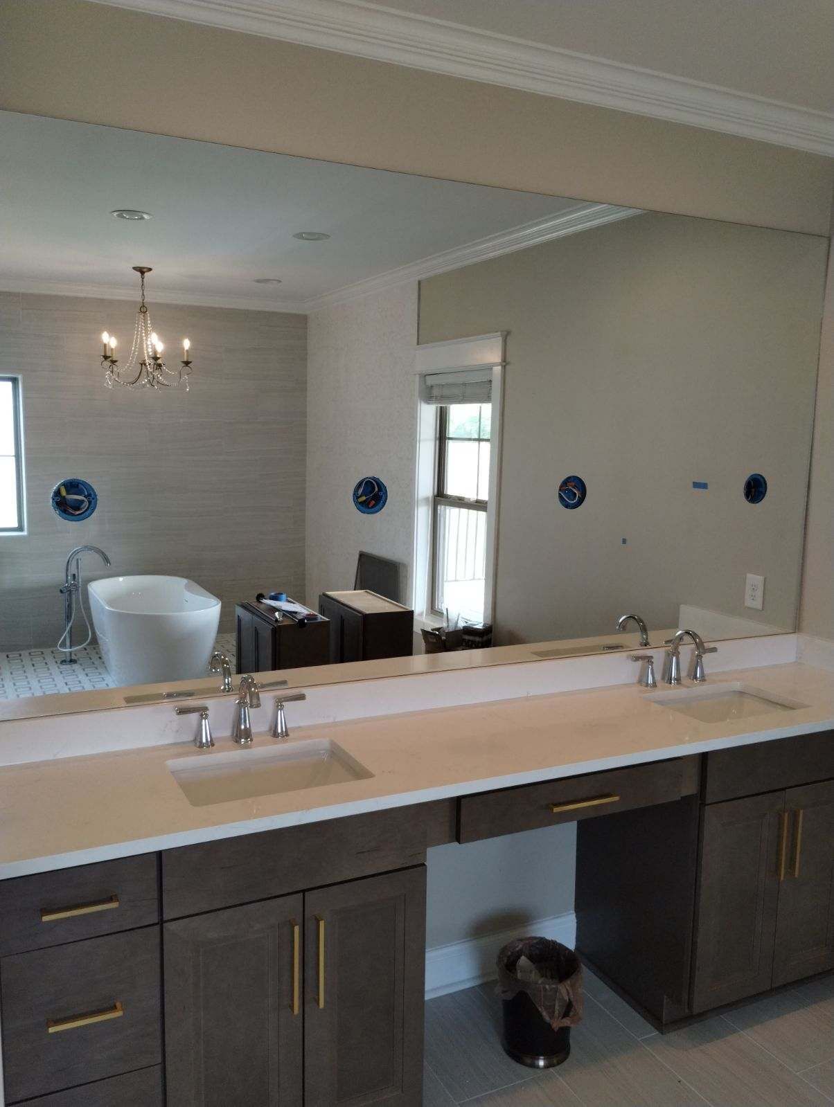 A double-sink bathroom vanity with dark wood cabinets and a light countertop, facing a large wall mirror. 