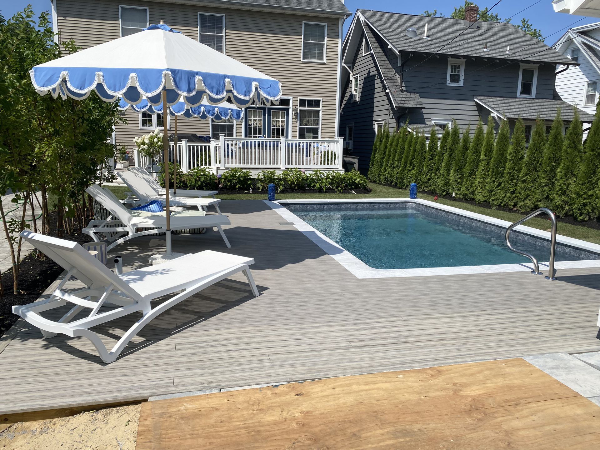 Backyard pool with white lounge chairs, blue umbrella, and house patio overlooking the water