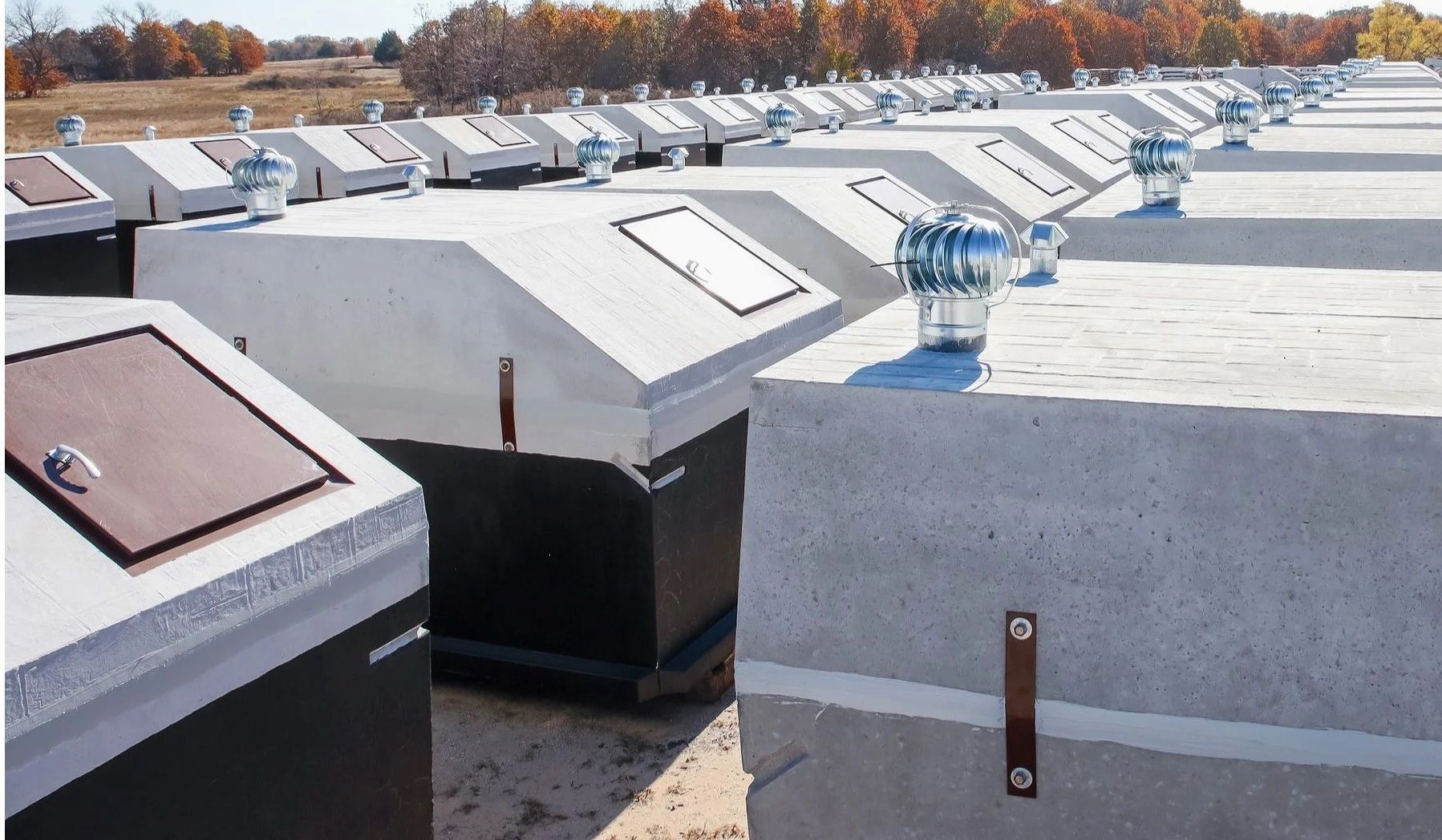 Rows of gray concrete enclosures on a rooftop, each with a metal hatch and vent.