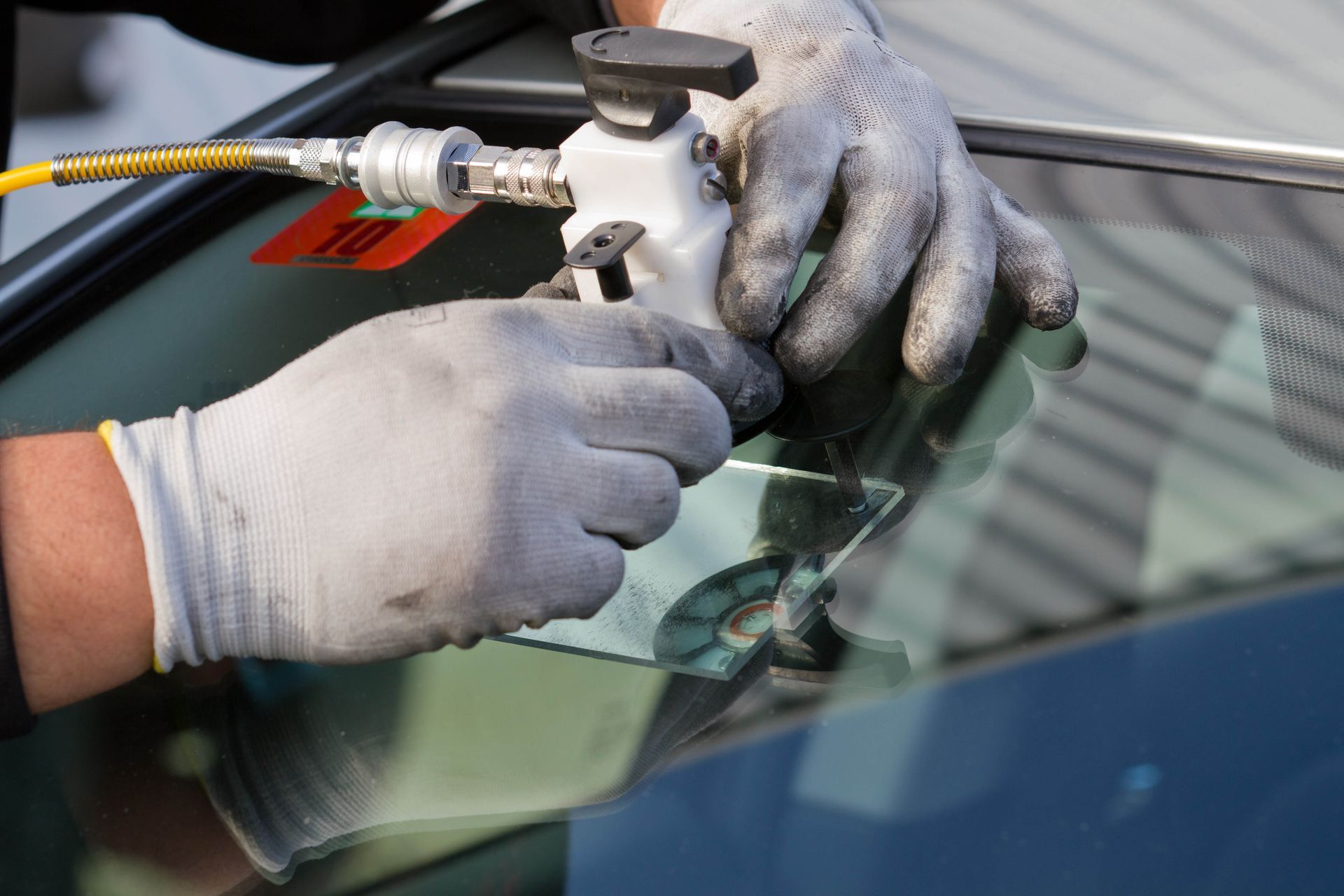 Gloved hands repairing a car windshield crack with a tool and adhesive
