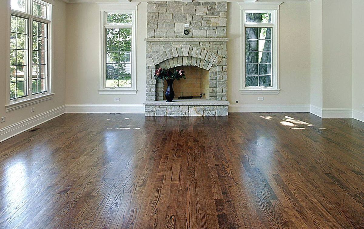 Empty living room with polished hardwood floors and a stone fireplace between tall windows