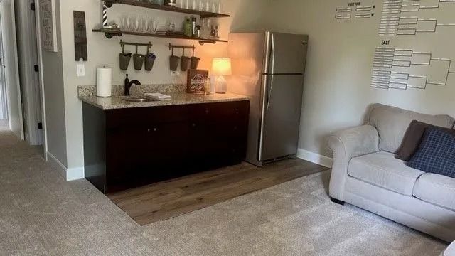 Cozy living room with sofa, dark sideboard, lamp, floating shelves, and stainless steel refrigerator next to kitchen area