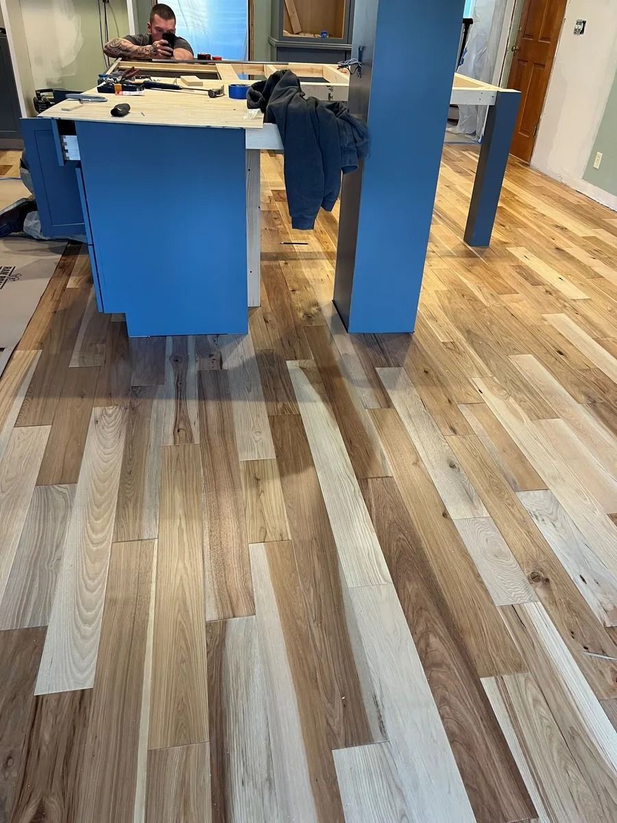 Empty office with a blue table, wood floor, and a person working at the back.