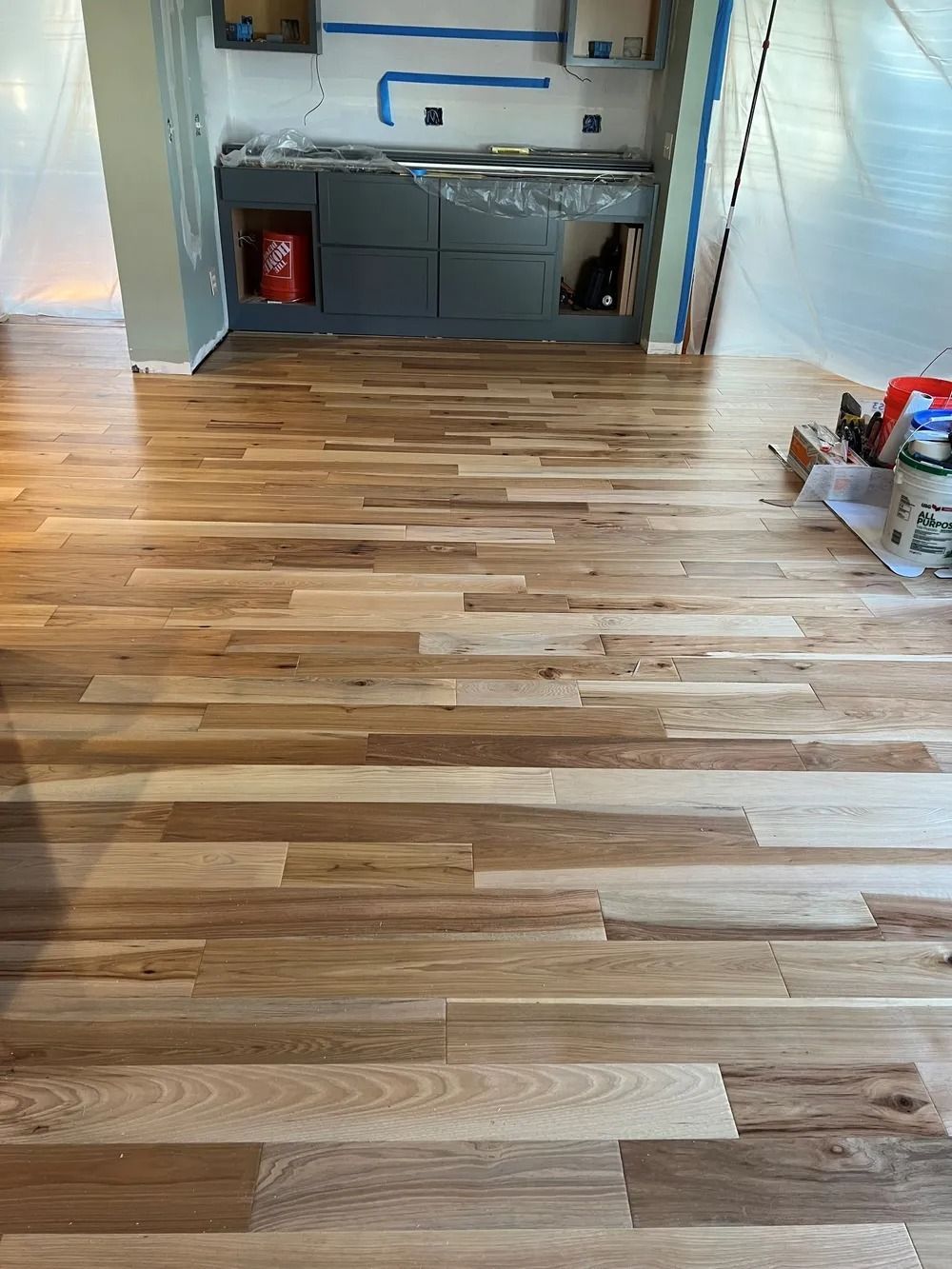 Wood-look hardwood floor leading into a small kitchen with gray cabinets and a red fire extinguisher.