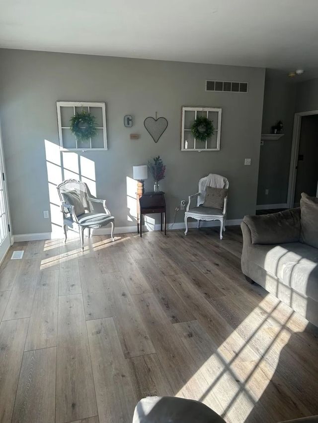 Sunlit living room with gray walls, two white chairs, wall art, and a couch on wood flooring