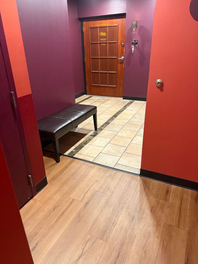 Hallway with red walls, wooden door, tiled entryway, and a black bench on the left.