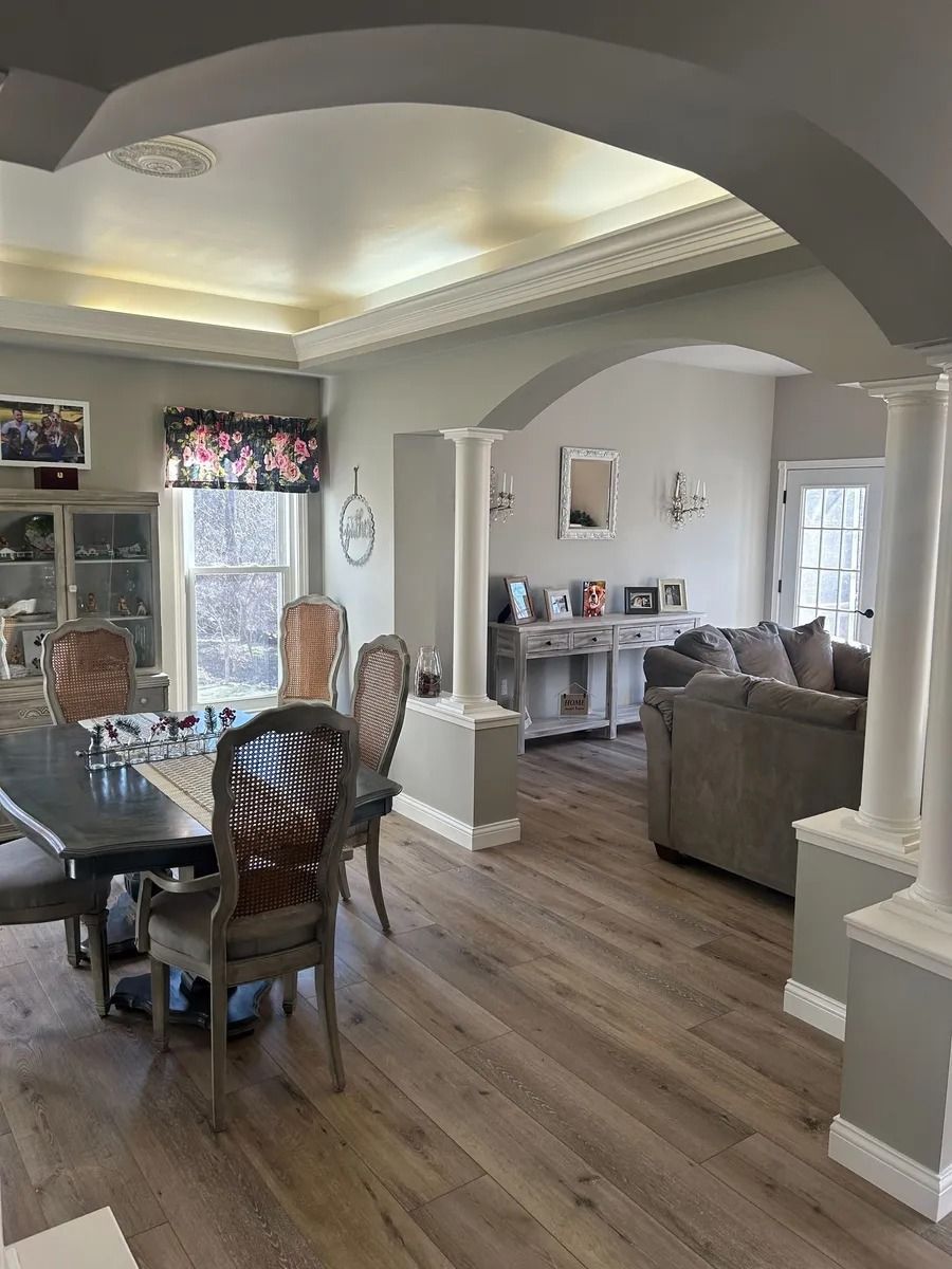 Open-concept dining and living room with arched ceilings, wood floors, and gray furniture.
