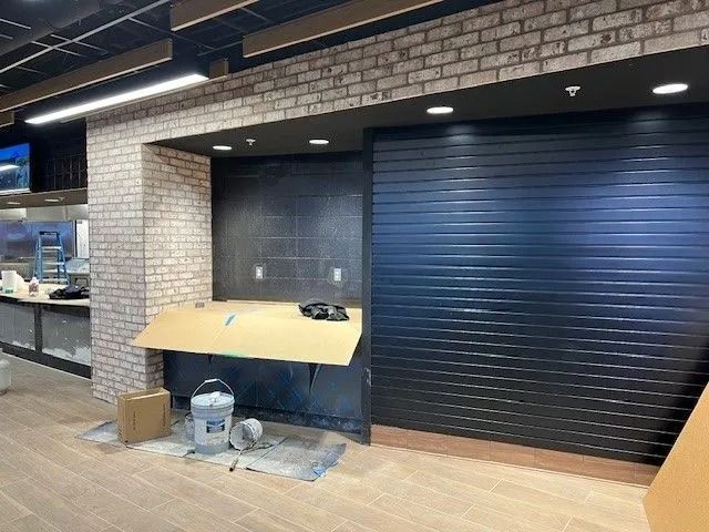 Construction site with a black roll-up shutter, brick wall, and a work table covered in protective plastic.